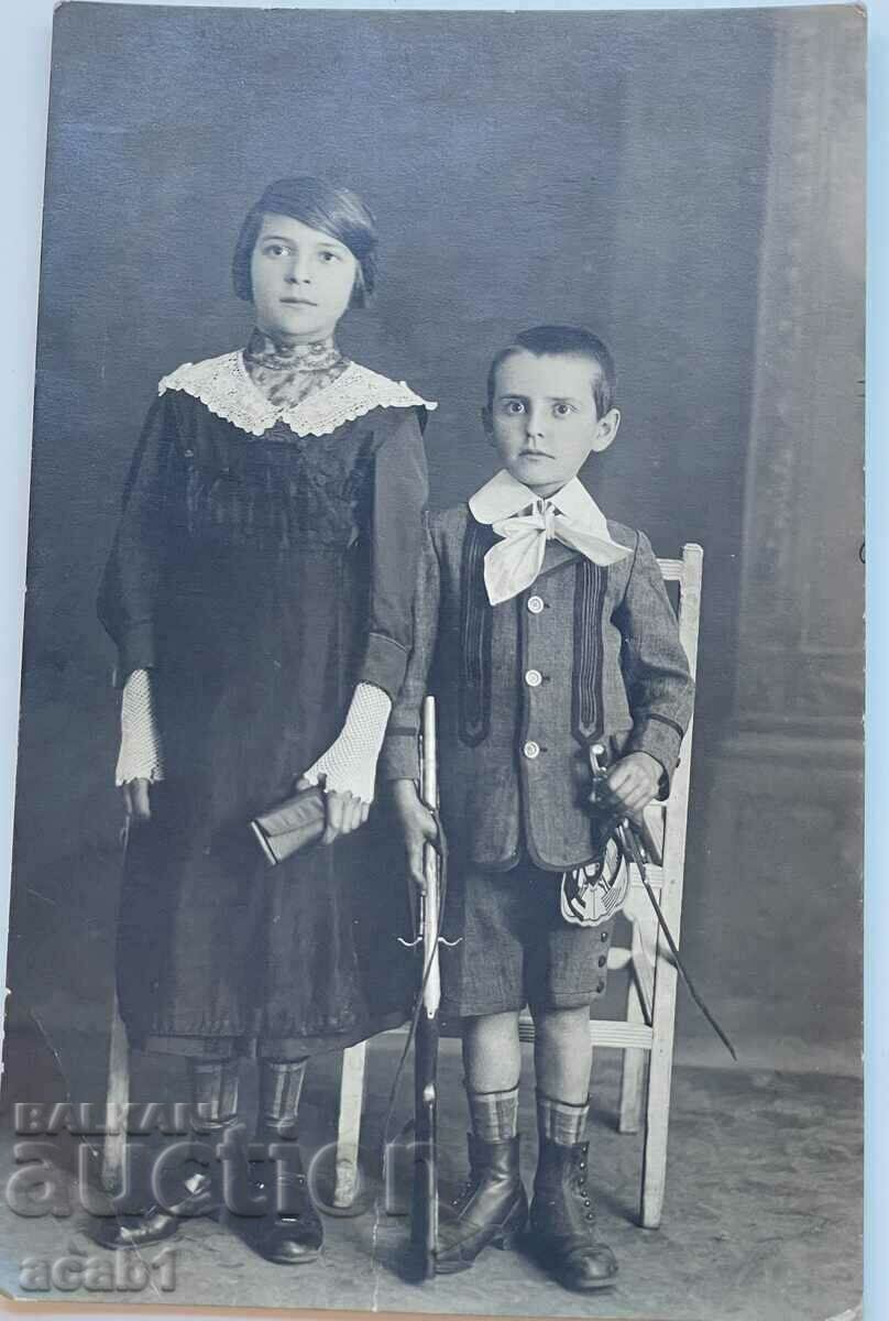 Copii într-o fotografie cu o pușcă și o sabie