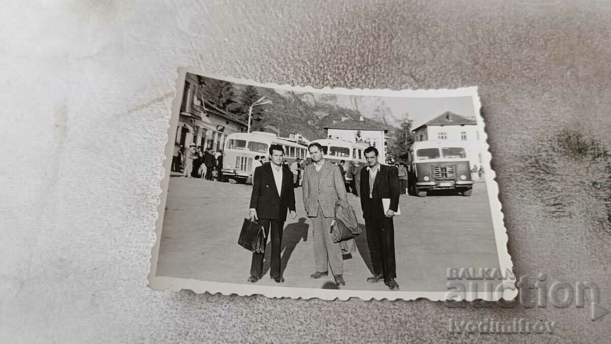 Foto Trei bărbați într-o piață în fața a trei autobuze de epocă