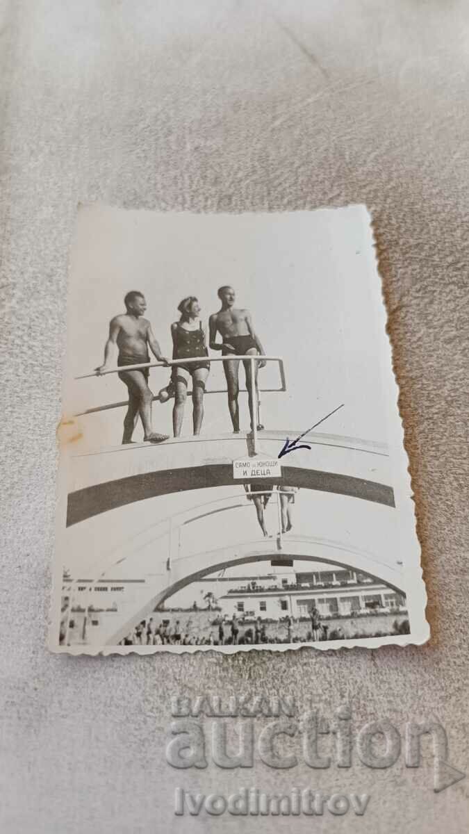 Foto Doi tineri și o fată pe un pod lângă piscină