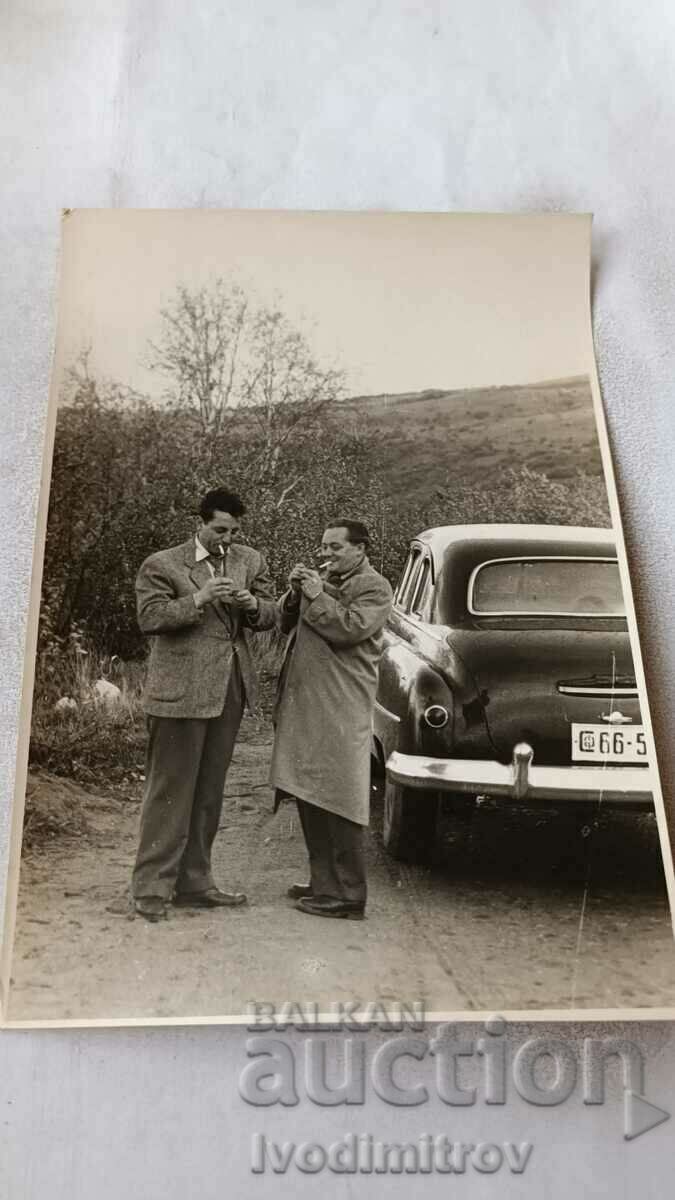 Photo Two men lighting cigarettes next to a vintage car 1955