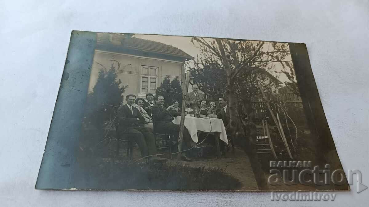 Photo Men and women at a table in the yard of their house, 1928