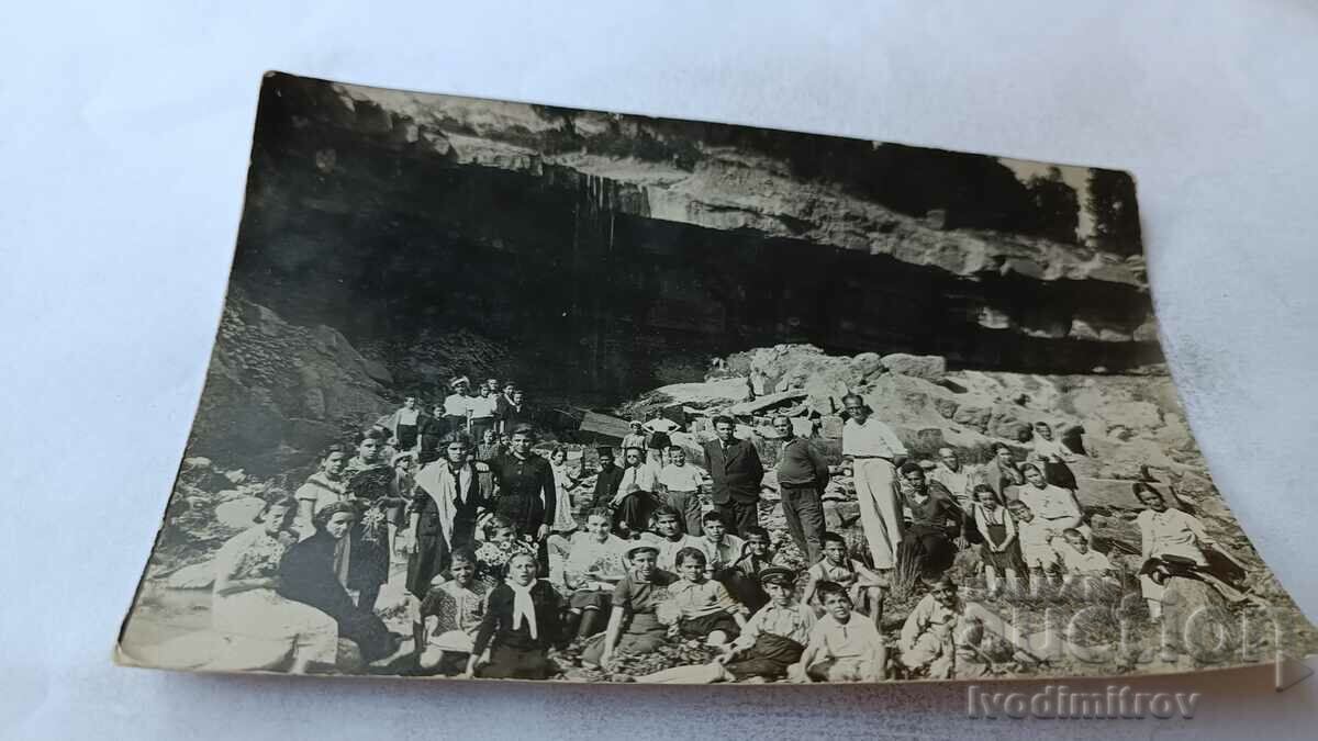 Photo Men, women and children in front of a cave