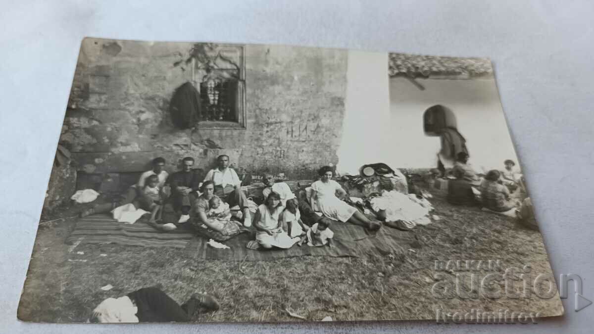 Снимка Мъже жени и деца седнали на черги на земята