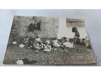 Снимка Мъже жени и деца седнали на черги на земята