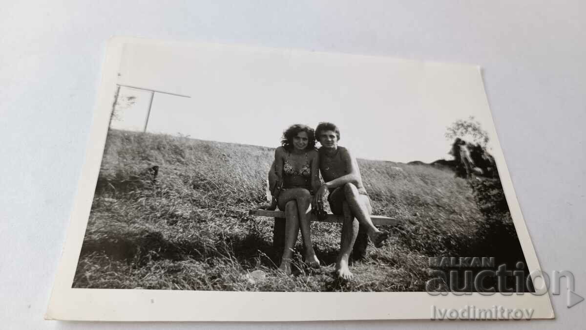 Photo A young man and a girl in a swimsuit on a wooden bench