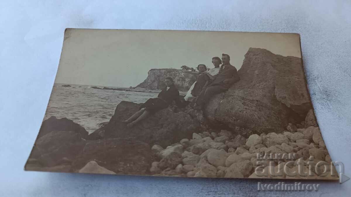 Photo A man and three young women on rocks above the sea