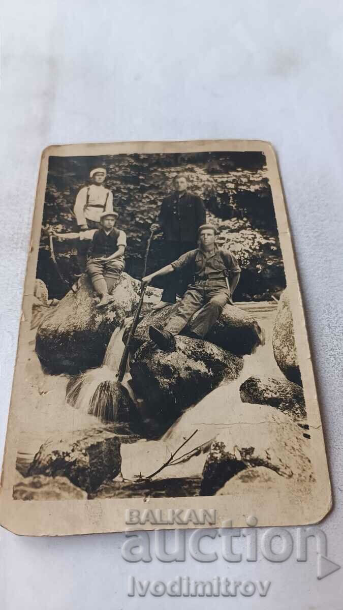 Photo A soldier and three young men on rocks in a raging stream