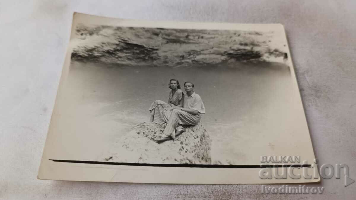 Picture A man and a woman sitting on a rock by a river