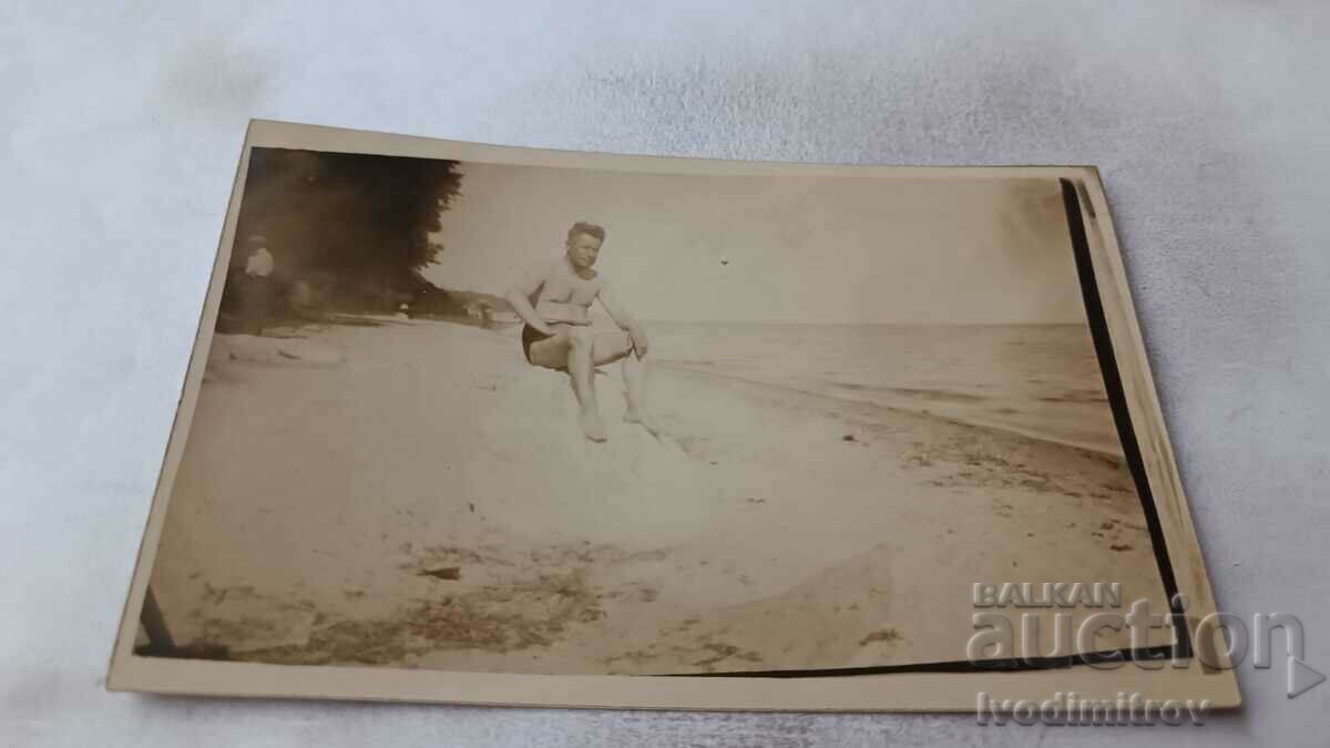 Photo A man in a vintage swimsuit sitting on a stone on the seashore