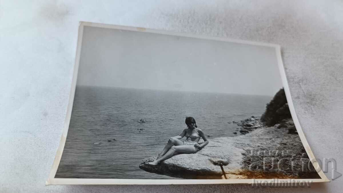 Снимка Млада жена по бански на скала на брега на морето
