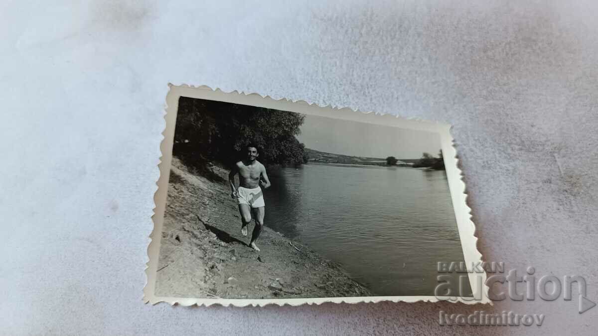 Photo Young man in shorts running along the river