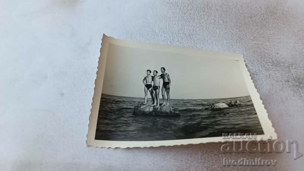 Photo Three young men in swimsuits on a rock in the sea