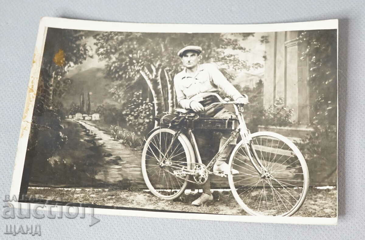 Fotografie de carte poștală din anii 1930 cu un bărbat cu o roată de bicicletă de epocă