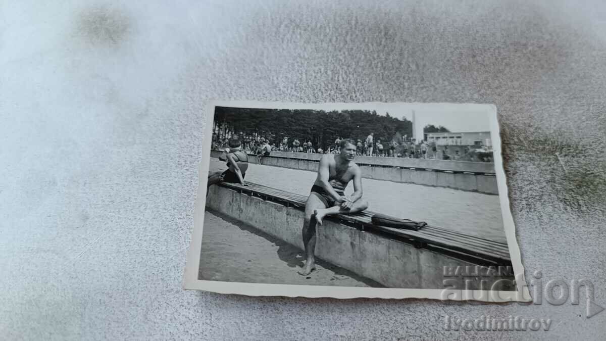 Photo A man in a swimsuit sitting on a wooden platform