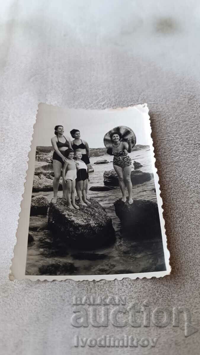 Photo Three women and two children in swimsuits on stones in the sea