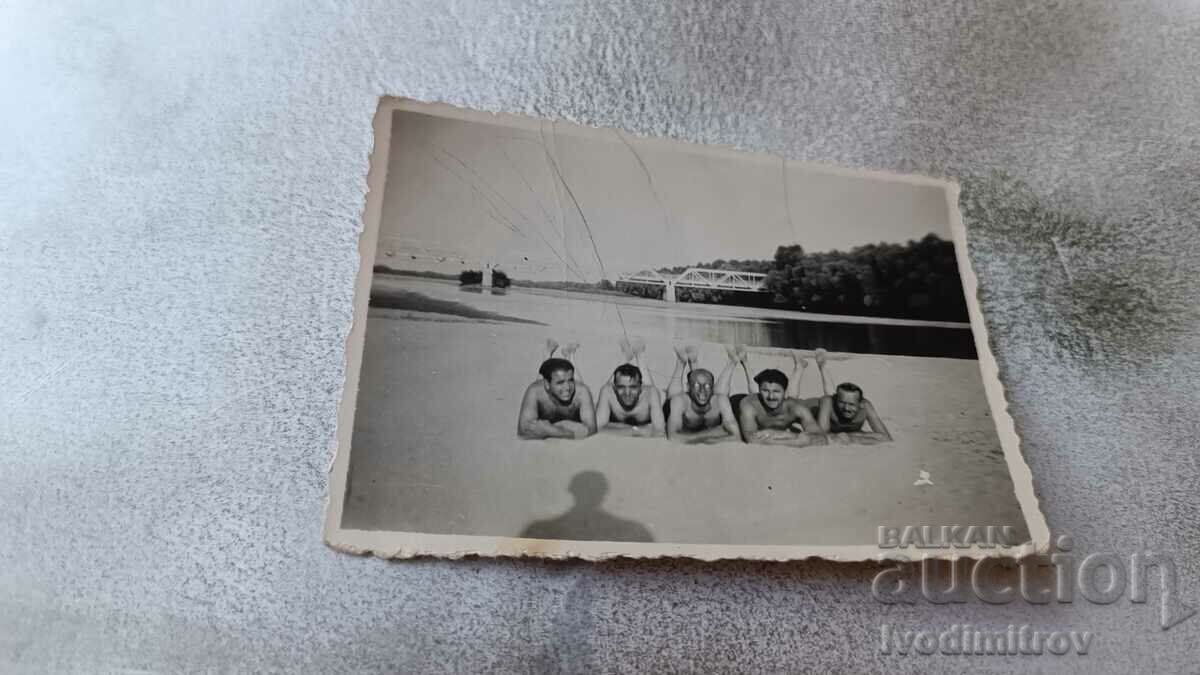 Imagine Cinci bărbați în costume de baie, întinși pe o plajă de lângă râu