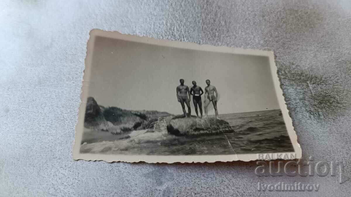 Photo Three men in swimsuits on a rock in the sea