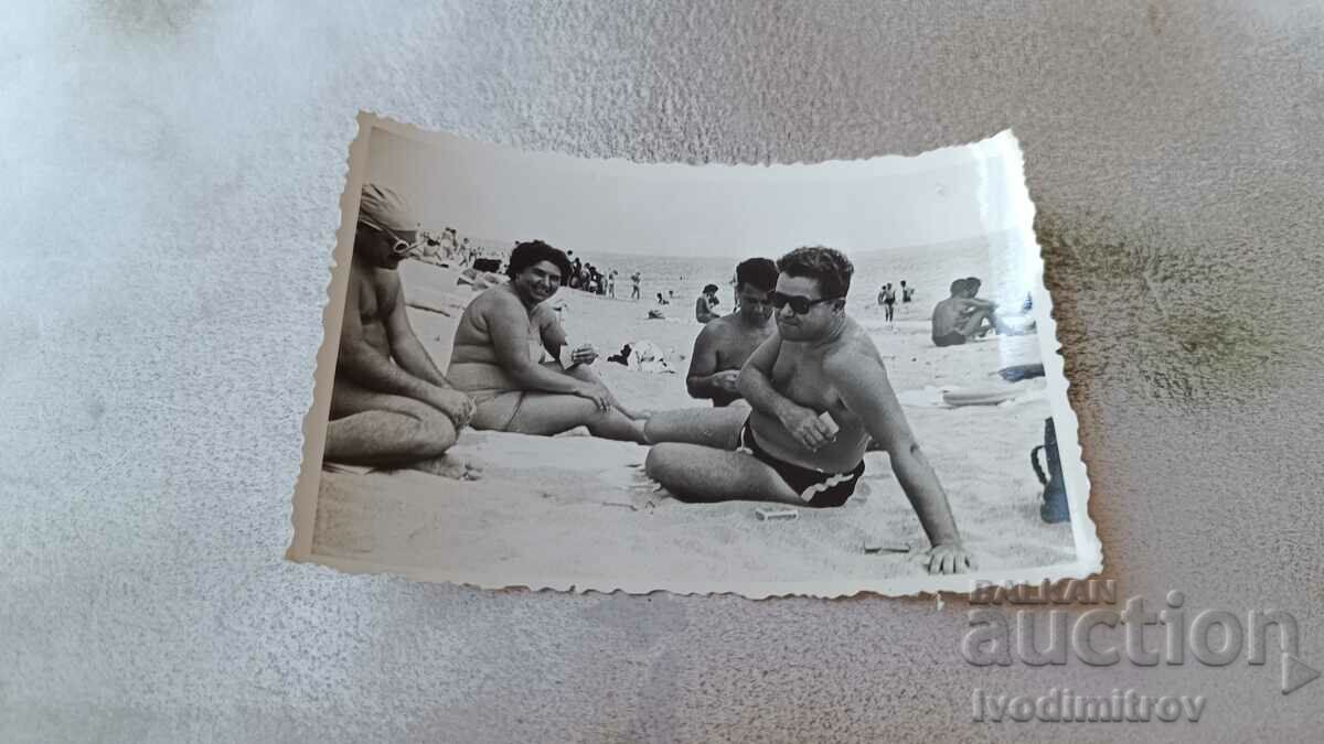 Photo Three men and a woman playing cards on the beach