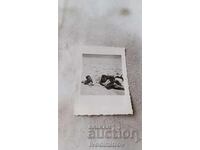 Photo of a young man and two young girls lying on the beach