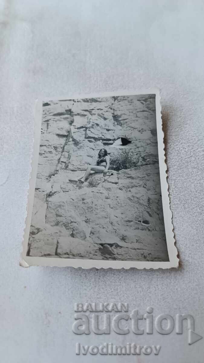 Φωτογραφία Νέας κοπέλας με μαγιό καθισμένη σε βράχο