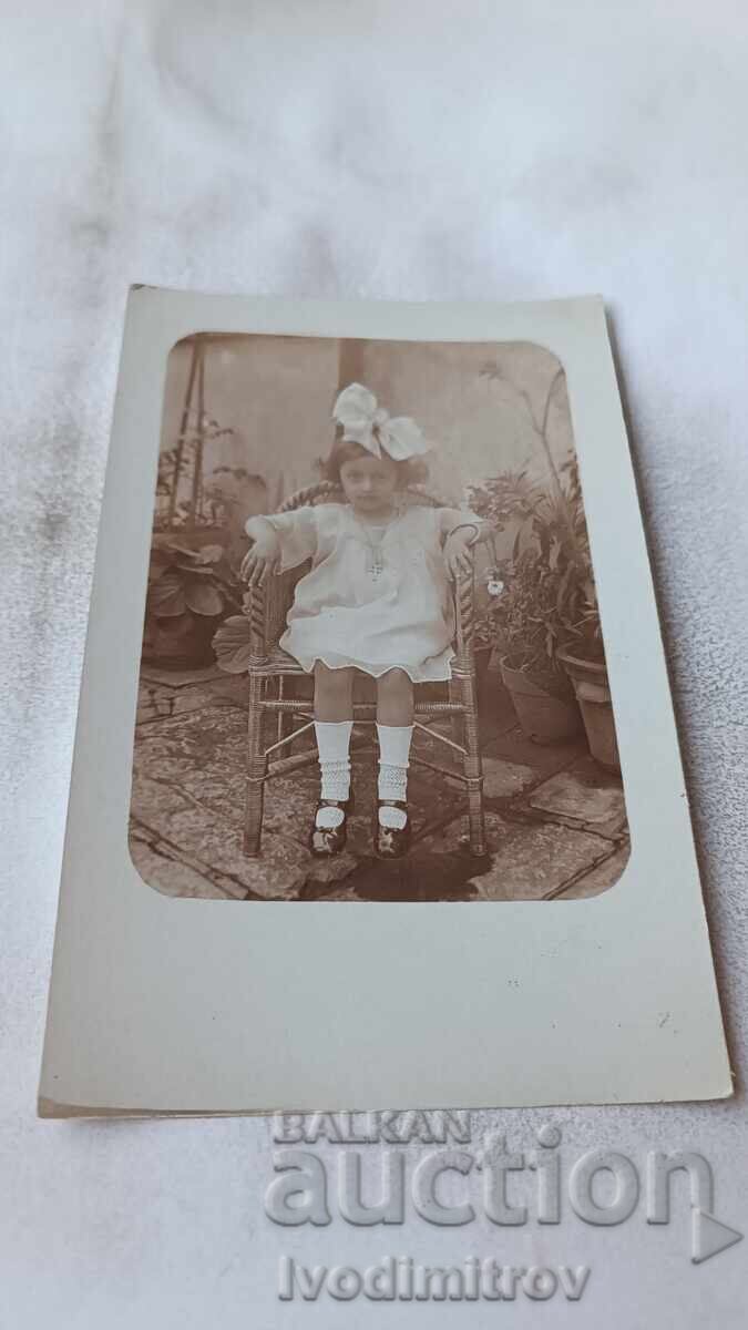 Снимка Момченце с бяла рокличка седнала на плетен стол