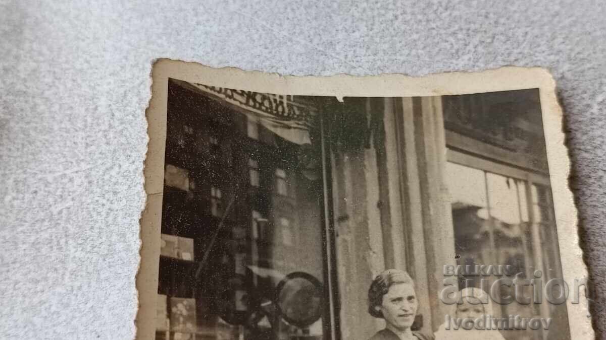 Fotografie Sofia Femeie cu bebeluș în fața a două magazine cu preț 2.65 BGN | € 1.35