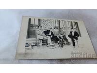 Fotografie cu patru bărbați stând pe scaune în fața unei clădiri