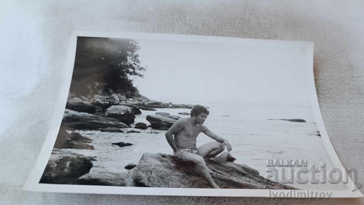 Φωτογραφία Άνδρας κάθεται σε βράχο δίπλα στη θάλασσα