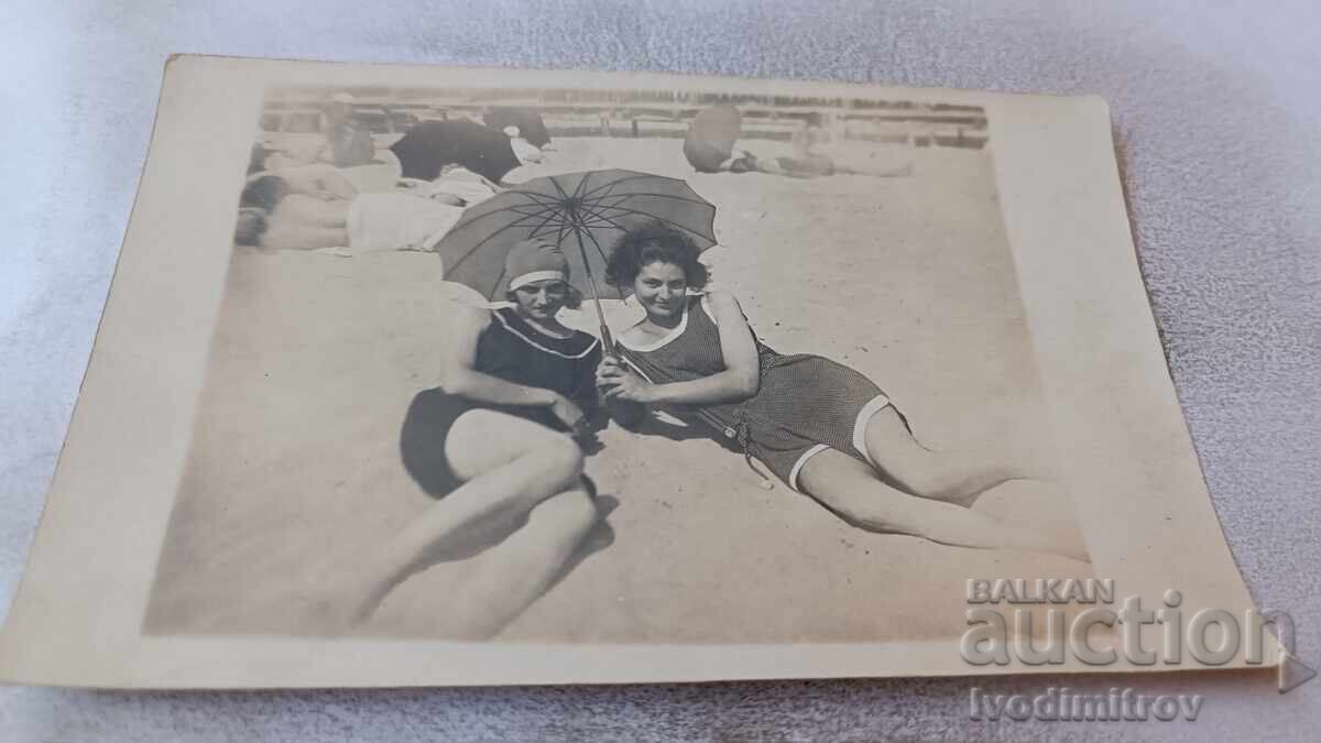 Φωτογραφία Δύο νεαρών κοριτσιών με ρετρό μαγιό και ομπρέλα στην παραλία