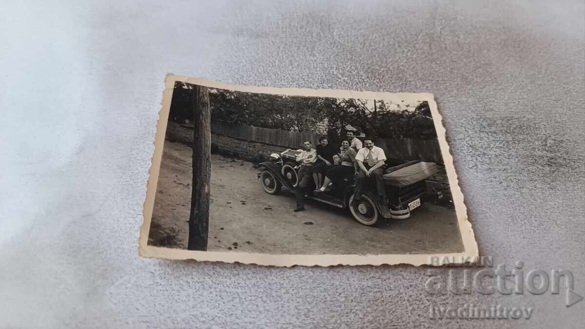 Φωτογραφία Άνδρες και γυναίκες με ρετρό αυτοκίνητο με αριθμό κυκλοφορίας Πλ 534