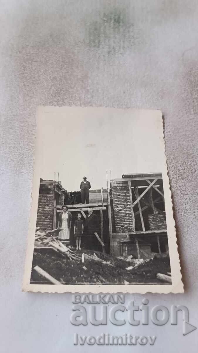 C-ca Bărbați, femeie și fată în fața unei case unifamiliale în construcție C-ca Bărbați, femeie și fată în fața unei case unifamiliale în construcție