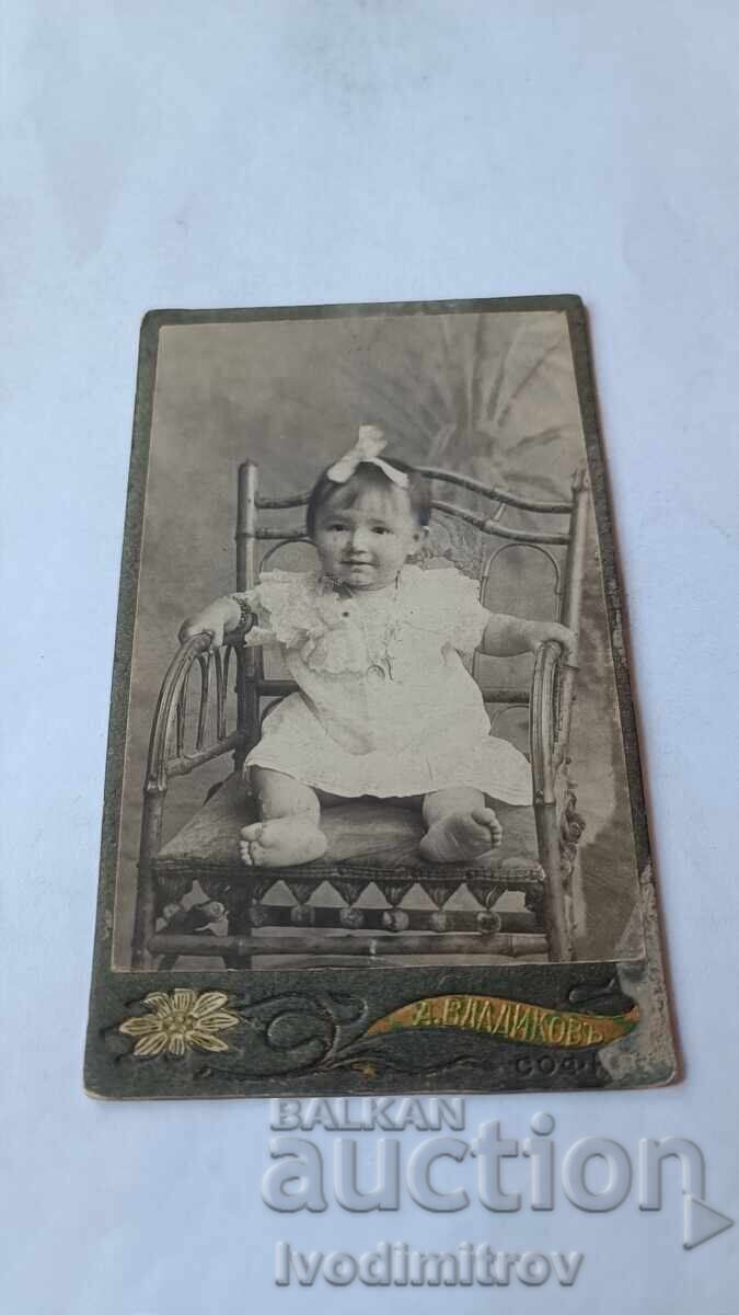 Снимка Малко момиченце в бяла рокличка на дървен стол Картон Снимка Малко момиченце в бяла рокличка на дървен стол Картон