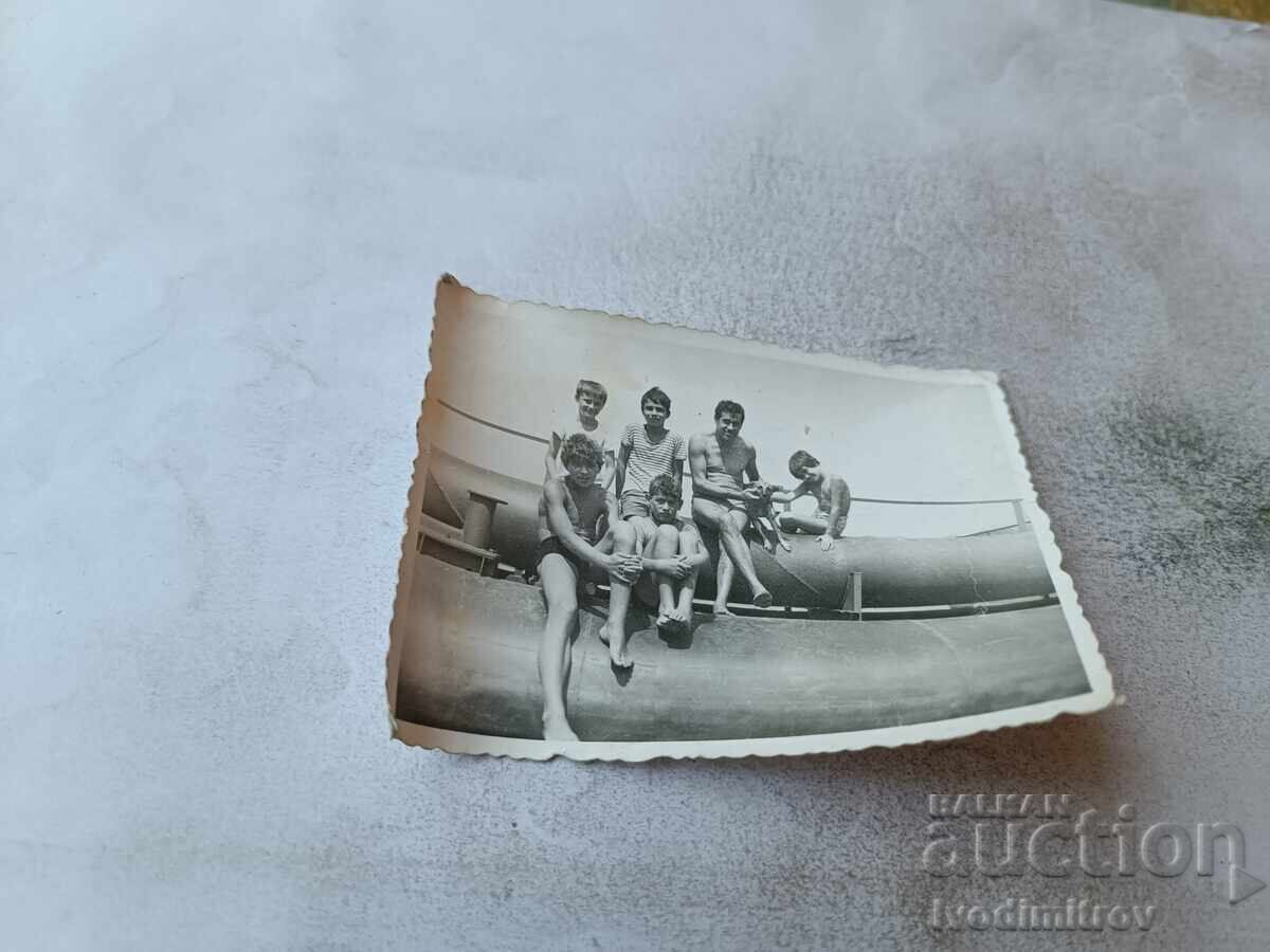 Photo Men and boys in swimsuits sitting on pipes