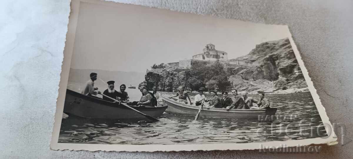 Photo of men, women, and a clergyman with boats on Lake Ohrid